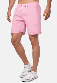 Pantaloni da bagno rosa con vita elastica, cordino bianco e tasche laterali. Presenta un logo sobrio bianco sulla parte anteriore.