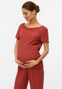 Haut de maternité en tissu texturé rouille, présentant un décolleté ondulé et des manches courtes, associé à un pantalon assorti à coupe ample.