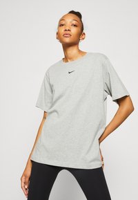 Camiseta de algodón gris con mangas cortas, cuello redondo y un pequeño logo negro de Nike centrado en el pecho. Textura suave y corte relajado.