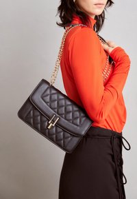 Czarna pikowana torebka na ramię z złotym zapięciem i łańcuszkowym paskiem, eksponowana na jednolitym tle, o prostokątnym kształcie i gładkiej fakturze.