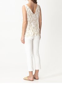 Haut blanc sans manches avec motif floral doré, col en V, associé à un pantalon blanc court et des sandales plates. Texture de tissu lisse.