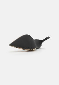 Sorte høye hæler med spiss tå, laget av teksturert materiale og med mønstret hæl i nyanser av gull og svart.