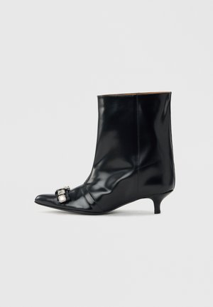 Black leather ankle boot with pointed toe, low kitten heel, and decorative silver buckle on side near toe.