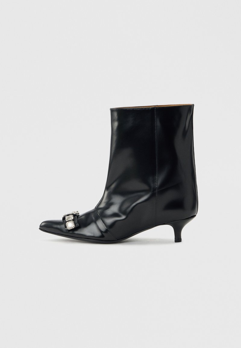 Μαύρο δερμάτινο μποτάκι αστραγάλου με μυτερή μύτη, χαμηλό τακούνι στιλέτο και διακοσμητική ασημένια αγκράφα στο πλάι κοντά στη μύτη.