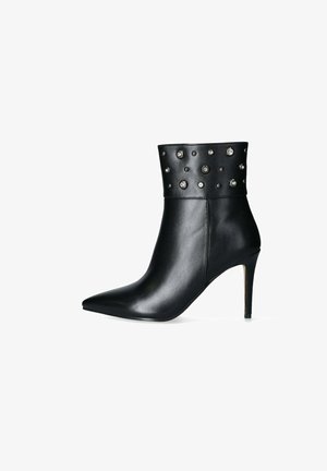 Stivale alla caviglia nero in pelle liscia, con punta affusolata, tacco alto sottile e borchie decorative in argento sul gambale.