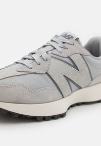 Grå jogging-sko laget av semsket skinn og mesh-materialer, med et fremtredende "N"-logo, lisser og en gummisåle med grep mønstre.