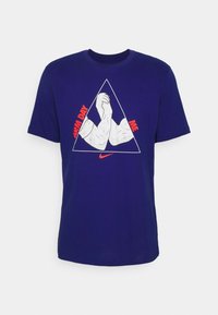 Tummansininen puuvillapaita, jossa on graafinen kuva kahdesta joustetusta kädestä kolmiomaisessa muodossa, ja punainen teksti "ARM DAY ME" sekä Nike-logo.