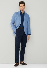 Ljusblå linn blazer över en mörkblå skjorta, tillsammans med marinblå byxor och bruna loafers. Enkelt mönster, skräddarsydd passform och kontrasterande färger.