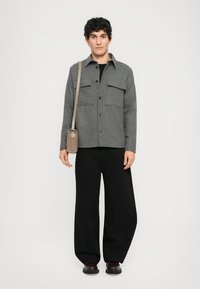 Gray button-up jacket with two chest pockets, worn over a black shirt and black wide-leg pants. The model carries a small beige crossbody bag.