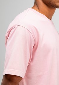 Lichtroze T-shirt met korte mouwen, gemaakt van zachte stof, met een ronde halslijn en versterkte naden langs de schouders.