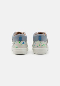 Hellblaue Sneakers mit einem strukturierten Mesh-Obermaterial, weißer Gummisohle und spritzfarbigen Mustern in Blau und Grün an der Ferse und den Seiten.