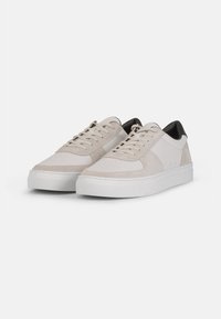 Hellgraue Sneakers aus glattem Leder und Wildleder, mit einer dicken weißen Sohle und einem kontrastierenden schwarzen Fersenakzent.