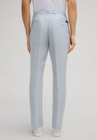 Jasnoniebieskie lniane spodnie o teksturowanym wykończeniu, z podwójnymi tylnymi kieszeniami i widocznym przeszyciem, zestawione z białymi trampkami.