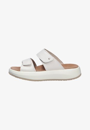 Helle beige Slipper mit zwei verstellbaren Klettverschlüssen, weichem Leder-Obermaterial, gepolstertem Innensohle und einer dicken weißen Gummisohle.