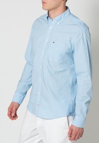 Hellblau karierte Button-down-Hemd aus Baumwolle. Verfügt über einen Kragen, eine Brusttasche und ein dezentes Logo-Detail auf der linken Seite.