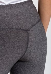 Närbild av en person som bär högmidjade, mörkgrå, åtsittande träningsleggings med synlig sömnad.