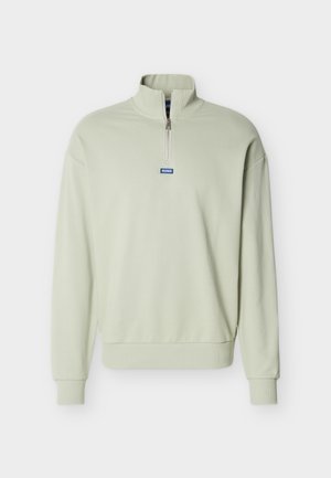 Ανοιχτό πράσινο πουλόβερ με μακριά μανίκια και φερμουάρ τριμήνου, με μπλε ετικέτα «HUGO» στο κέντρο κάτω από το φερμουάρ στο στήθος.