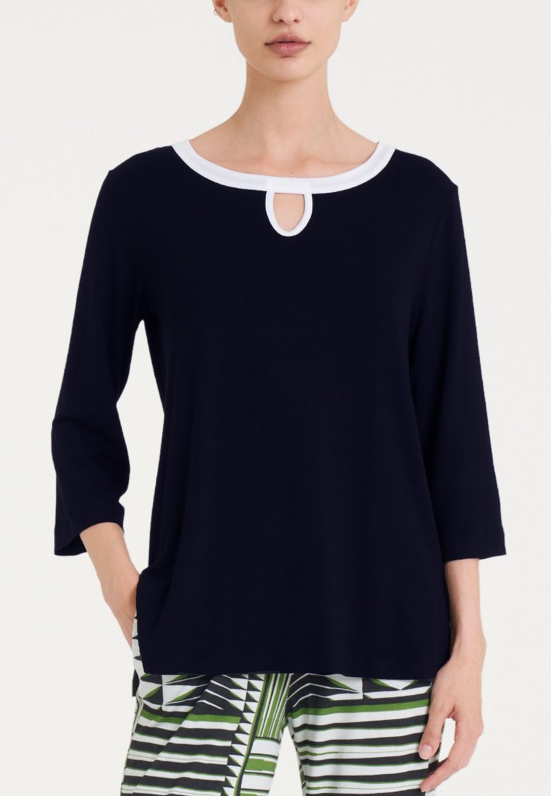 Camicia blu navy con maniche a tre quarti. Collo rotondo con bordino bianco e dettaglio a chiave. Tessuto morbido e liscio, vestibilità rilassata.