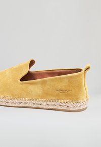 Żółta zamszowa espadrylka z plecioną podeszwą z juty oraz napisem „Fred Martin Collection” z boku, widziana z lewego profilu.
