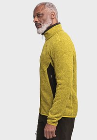 Gelbe Fleecejacke mit hohem Kragen, seitlichen Reißverschlusstaschen und kontrastierenden schwarzen Akzenten. Strukturiertes Material mit figurschmeichelndem Design.