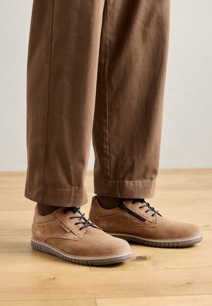 Pruun nubukist nööriga kingad tekstureeritud pinnaga, tumedate siniste nööride ja kummitaldaga, ühendatud pruunide pükstega.