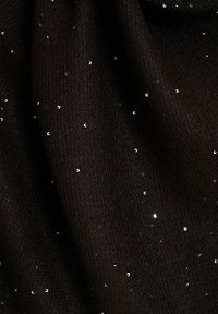 Tissu noir présentant une surface texturée avec des paillettes métalliques dispersées, créant un effet scintillant contre le fond sombre.