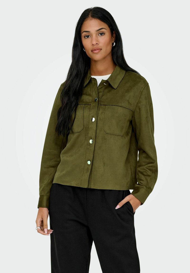 Olive green, suede shirt jacket with a collar, front pockets, and snap buttons. Worn with black, loose-fitting pants.