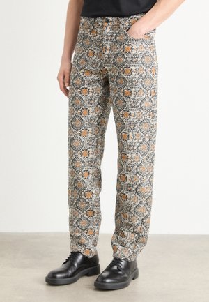 Osoba nosząca spodnie z wysokim stanem w czarno-biało-pomarańczowy wzór kwiatowy, w połączeniu z czarnymi skórzanymi butami sznurowanymi.