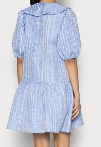 Vestido azul a rayas con mangas abullonadas, un cuello con volantes y un dobladillo en capas. Hecho de una tela liviana, con cierre de botones en la parte posterior.
