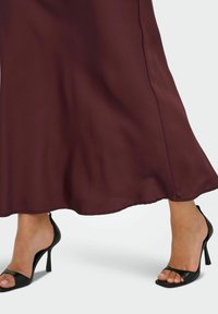 Burgundy satin maxiklänning med en flödande silhuett, parat med svarta öppna tå högklackade skor med tunna remmar och en elegant stilettklack.