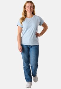 T-shirt azzurro chiaro a maniche corte con scollo rotondo, abbinato a jeans blu. Il modello indossa sneakers bianche. Design semplice.