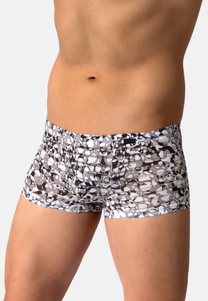 Männlicher Oberkörper mit eng anliegenden schwarz-weißen abstrakt gemusterten Boxershorts vor einfachem Hintergrund.
