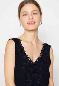Vestido preto sem mangas com um decote em V profundo adornado com intrincados bordados florais e uma textura de tecido suave.