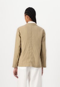 Veste en lin kaki avec un col, des manches longues et une finition légèrement texturée ; présente une couture au centre du dos et un design minimaliste.