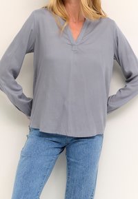 Graue Bluse mit langen Ärmeln und V-Ausschnitt, leichtes Material, lockere Passform und gerader Saum, kombiniert mit Jeans in mittlerer Bundhöhe.