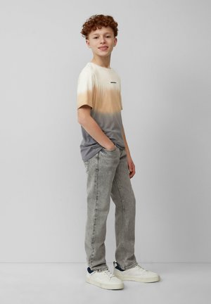 Korte mouwen T-shirt met een ombre kleurverloop van beige naar grijs, gecombineerd met lichtgrijze jeans en witte sneakers met marineblauwe accenten.