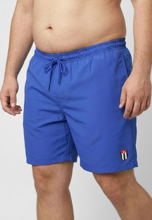 Mand iført lyseblå badeshorts med elastisk taljebånd og snøre, cubansk flagemblem på venstre ben.
