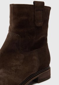 Hnědé semišové kotníkové boty s zaoblenou špičkou, jemným prošíváním, malým poutkem a vrstveným podpatkem. Hladká textura, klasický design.