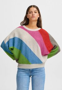 Pull oversized coloré avec des rayures diagonales audacieuses en rose, bleu, vert et rouge. Texture douce avec un ourlet côtelé et des manches larges.