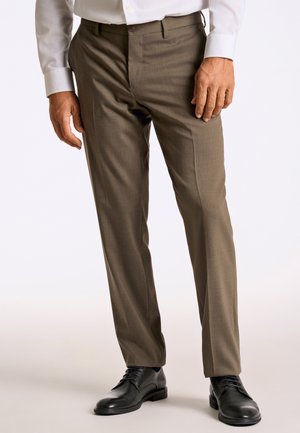 Bruine broek met een gladde textuur, rechte pijpen, platte voorkant en riemlussen, gecombineerd met zwarte leren schoenen.