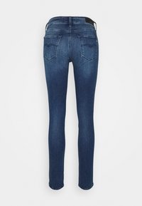Jeans ajustados en denim azul oscuro, con dos bolsillos traseros con un diseño sutil. La tela tiene una textura suave y un ligero estiramiento.