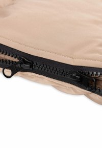 Coussin beige au toucher lisse, doté d'une fermeture éclair noire le long du bord, de coutures bordées et d'une apparence épaisse et moelleuse.