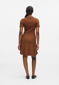 Pruun ribadega kudumisdress lühikeste varrukatega, kitsenev kehaosa ja laienev seelik. Omab ümmargust kaelust ja lainelist äärt. Kandsin musti jalatseid.