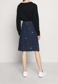 Denim A-line skirt with embroidered designs in various colors, paired with a black sweater. Includes a hemline detail with stitching.