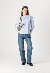 Blå stripete skjorte med volangdetaljer, parret med lyse denimjeans, svarte sko og en grønn skulderveske. Enkel, avslappet passform.