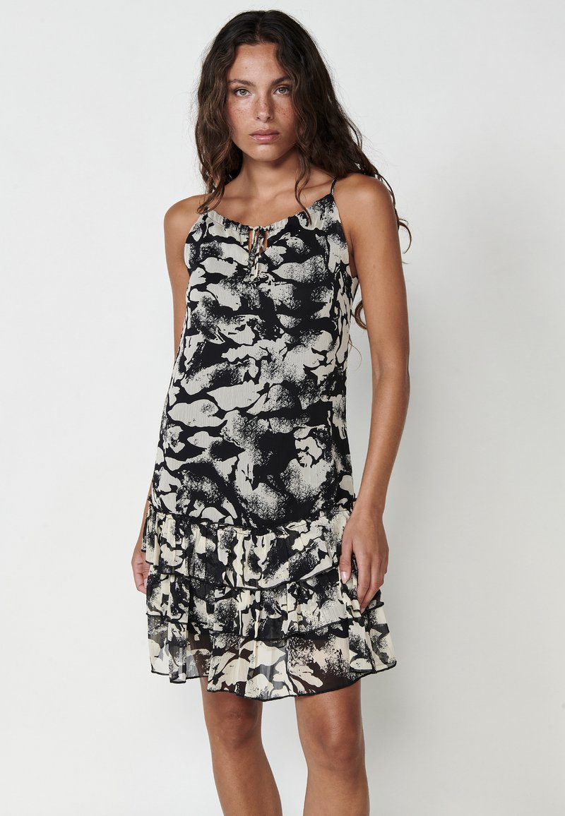 Schwarz-weißes Kleid mit floralem Muster, ausgestattete mit einem rüschenbesetzten Saum und verstellbaren Trägern, aus leichtem Stoff gefertigt.