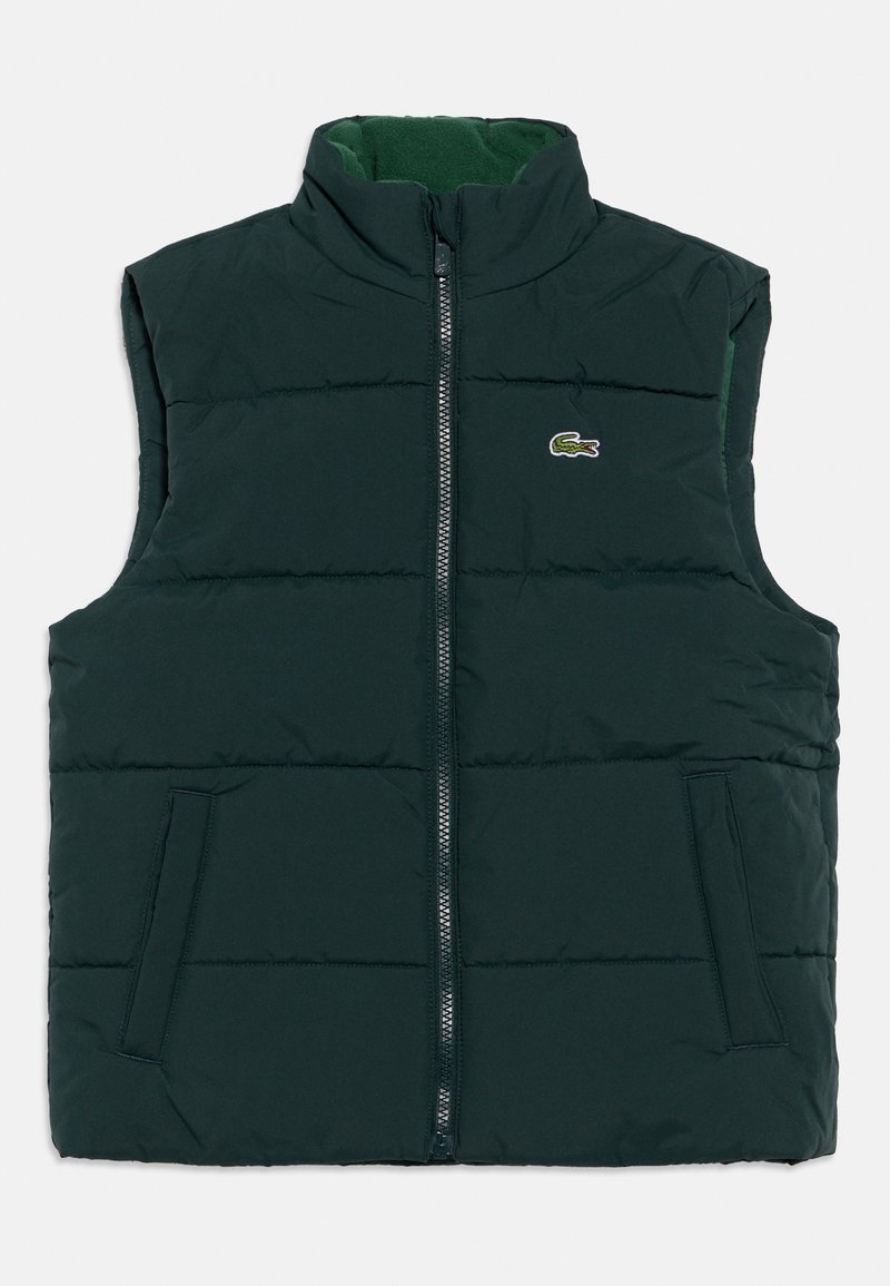 Αμάνικο ανδρικό γιλέκο με φουσκωτό ύφασμα σε σκούρο πράσινο. Διαθέτει ψηλό γιακά, εμπρόσθιο φερμουάρ, δύο πλαϊνές τσέπες και ένα μικρό λογότυπο στο στήθος.