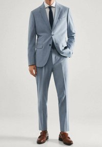 Un costume bleu clair avec une veste à un bouton et des revers crantés, associé à un pantalon assorti et des chaussures en cuir marron.