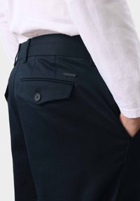 Schwarze Hosen mit glatter Oberfläche, ausgestattet mit Gesäßtaschen und einem kleinen Metallemblem mit der Aufschrift "AUTOGRAPH". Slim Fit mit modernem Schnitt.