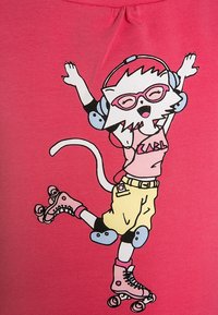 Růžová látka zobrazuje kreslenou kočku na kolečkových bruslích, která má na sobě sluchátka a růžové brýle, žluté šortky a chrániče kolen.